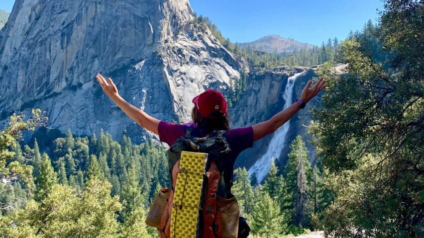A backpacker celebrates in front of Nevada Falls after hiking the John Muir Trail