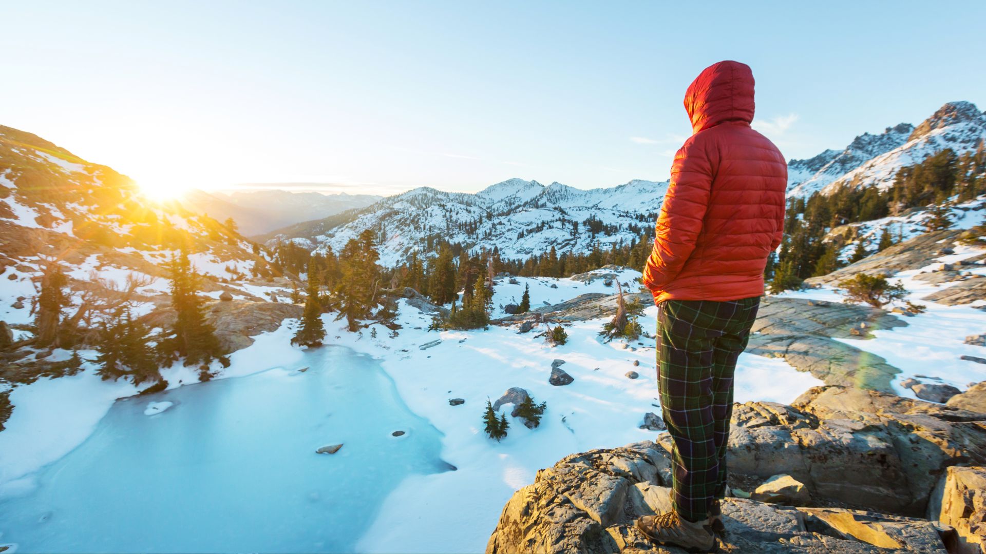A person in a puffy jacket looks out at a frozen alpine lake